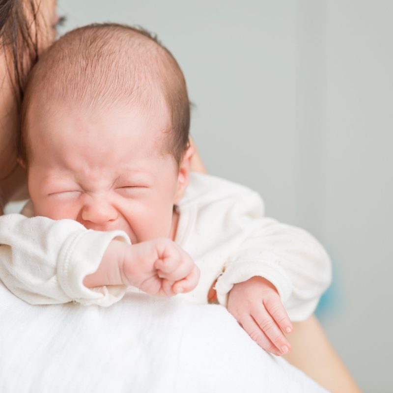 Newborn baby screaming in pain with colic on mother's shoulders
