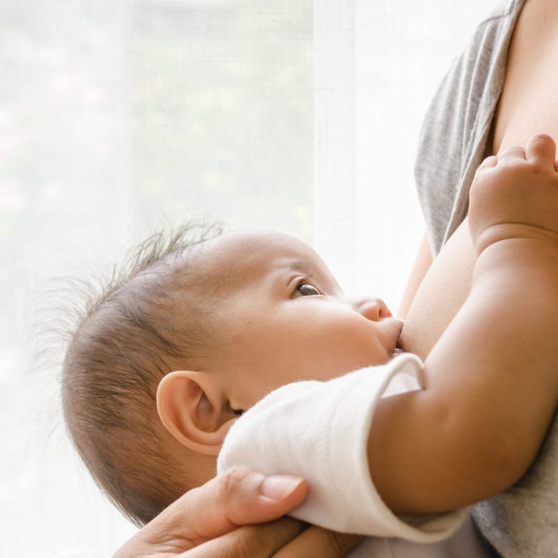 Mother breastfeeding her newborn baby beside window
