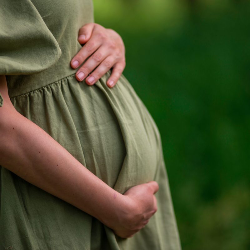 Caucasian Young Pregnant woman Tummy belly  summer green dress touching stomach field expecting a baby relaxing outside nature park lake rural Beautiful magic 8 months enjoying life glasses hat